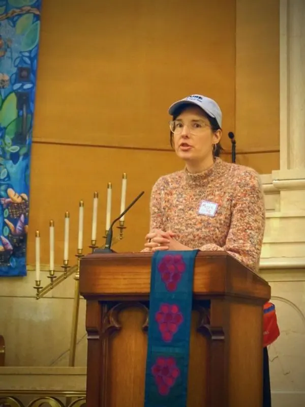 Maggie Schuppert, CURE's Campaigns Director, speaking from a podium at the Rise + Repair rally.