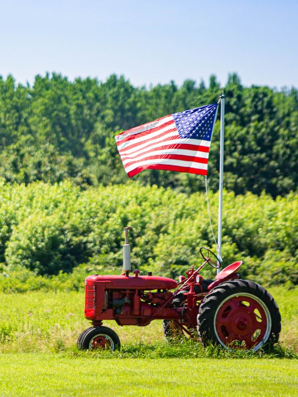 an American flag by an older red tractor