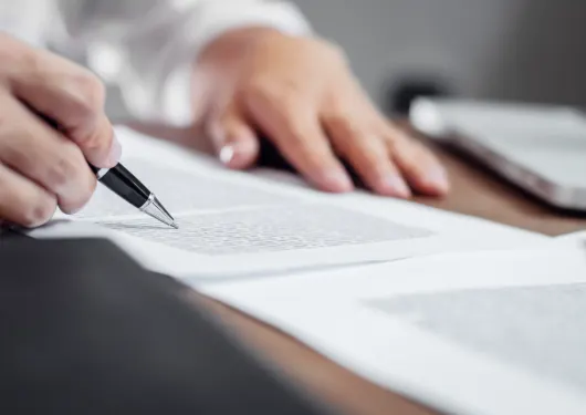 Two hands, one with a pen checking over a printed document