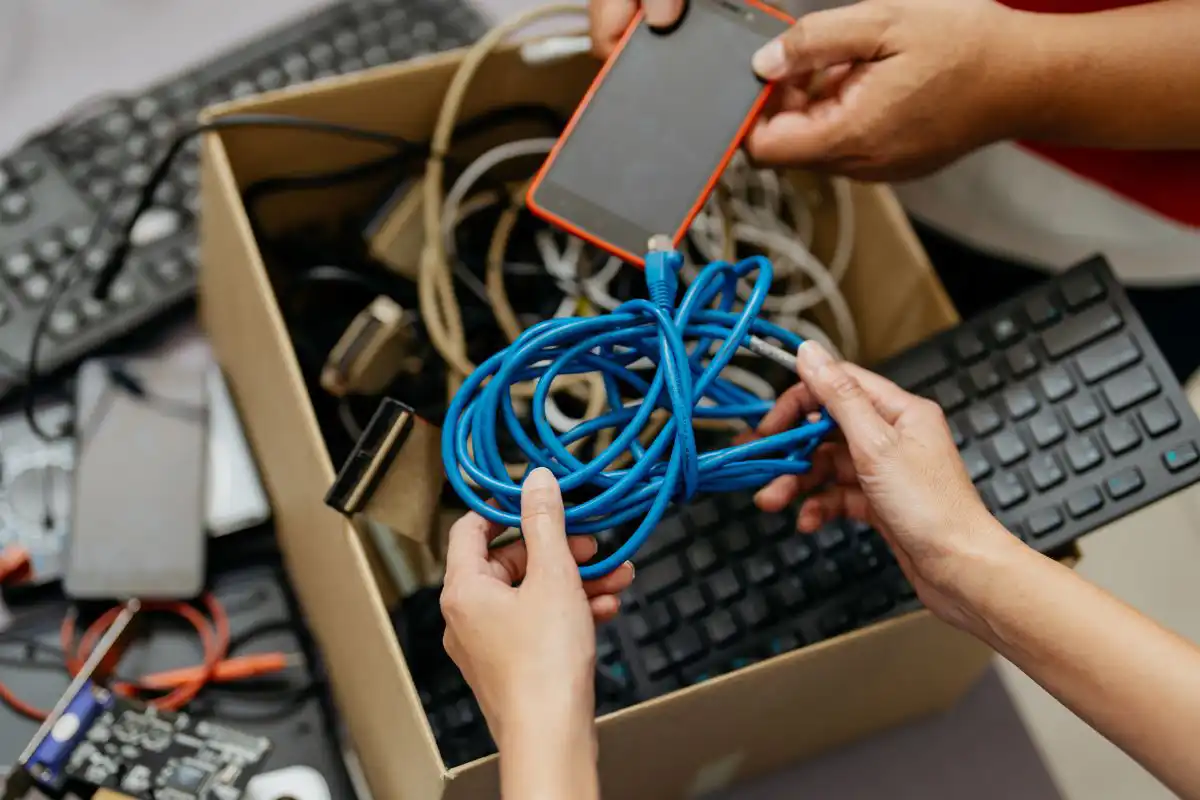 People with a box of old electronics including a blue cord, black keyboard and red smart phone