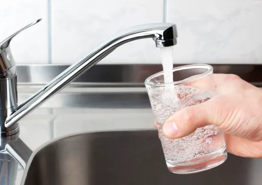 person filling a glass with water from a tap