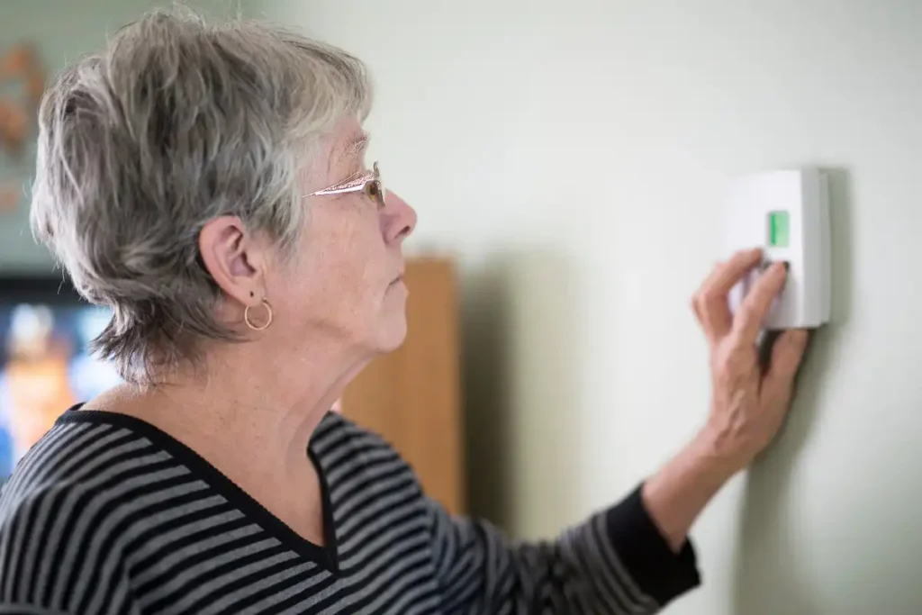 An older woman adjusting the thermostat