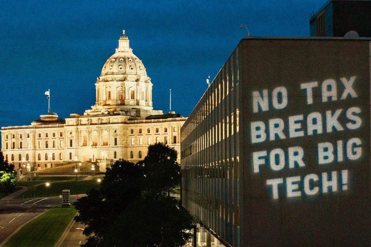 the MN state capitol at night with "no tax breaks for big tech" projected on a building